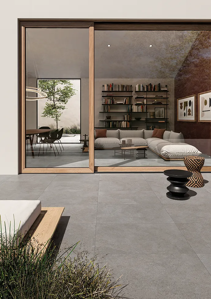 Diseño integrado de interior y exterior con baldosas de efecto piedra gris que unen un salón interior elegante con una terraza contemporánea, armonizando los espacios con estilo y continuidad.