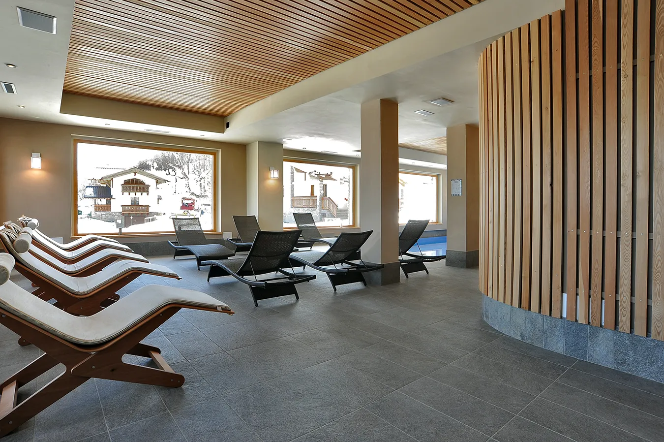 Hotel Sporting Prodongo SPA with elegant tiles, modern loungers, and large windows providing a charming view of the snowy locale.