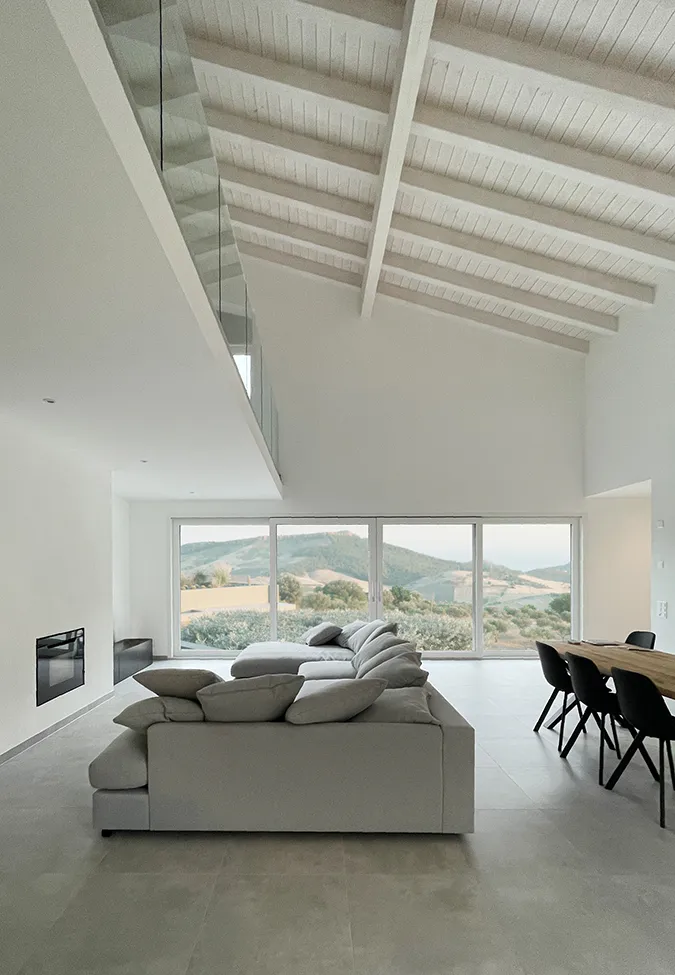 Sala de estar elegante con techos altos, grandes ventanas con vistas a colinas y azulejos de gres porcelánico efecto piedra gris de la colección Icon.