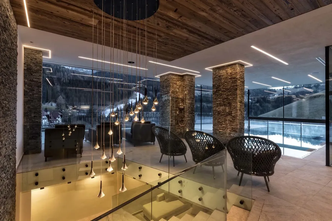Salon de montagne luxueux avec éclairage moderne, murs en pierre et vue panoramique enneigée.