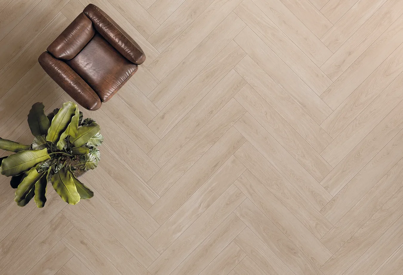 Luxury flooring with white herringbone wood-effect tiles from the Lineo collection, brown leather armchair, and green plant.