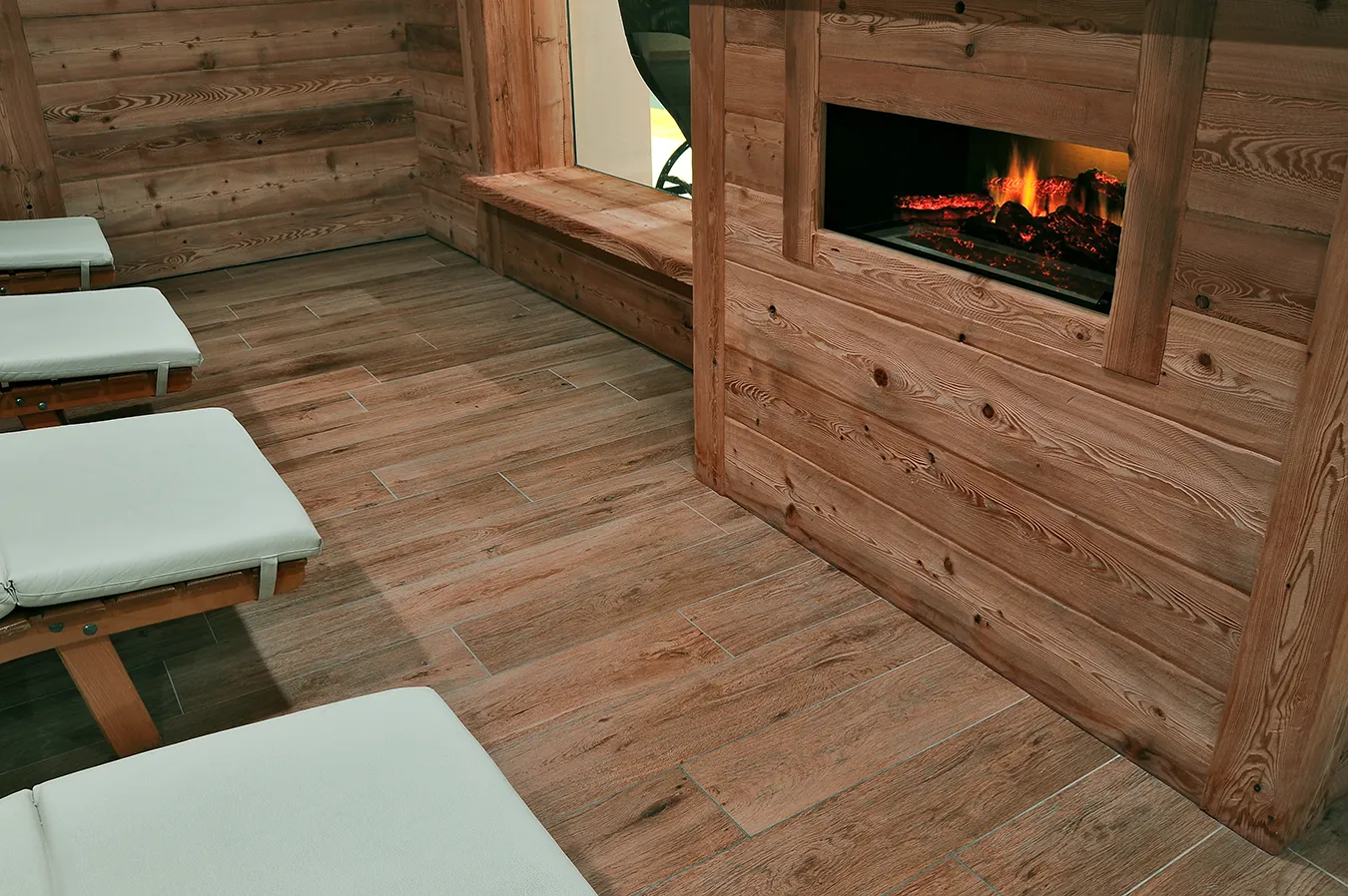Gemütliche Entspannungsecke mit Holzeffekt-Bodenbelag aus der Evoke Kollektion, der sich harmonisch in das rustikale Ambiente mit elektrischem Kamin einfügt, für eine warme und einladende Atmosphäre.