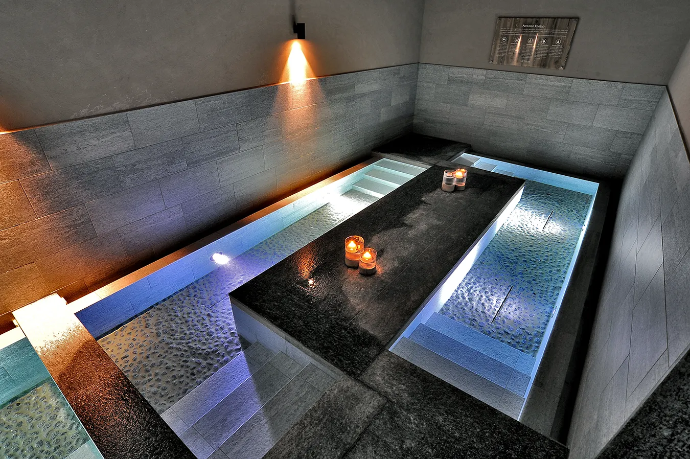 Stone-effect SPA flooring from the Percorsi Smart Pietra di Bagnolo collection, candlelit for a serene ambiance at QC Terme Dolomiti.