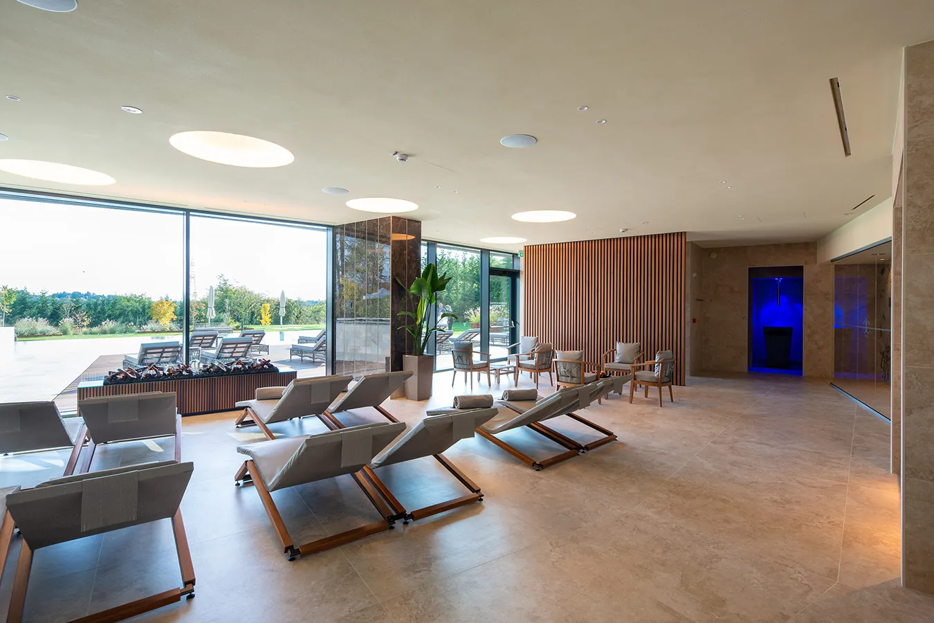 Amplio salón de SPA con elegantes azulejos de efecto piedra y mármol, grandes ventanas y cómodas tumbonas, para un ambiente relajante y de diseño.