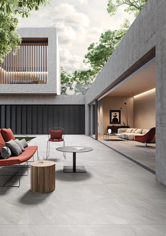 Area living esterna con piastrelle effetto pietra grigio, mobili moderni e aperture sul giardino.