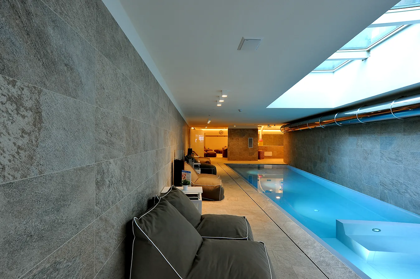 Area relax con piscina interna moderna con rivestimento in gres porcellanato grigio della collezione Percorsi Extra, colore Pietra di Combe.