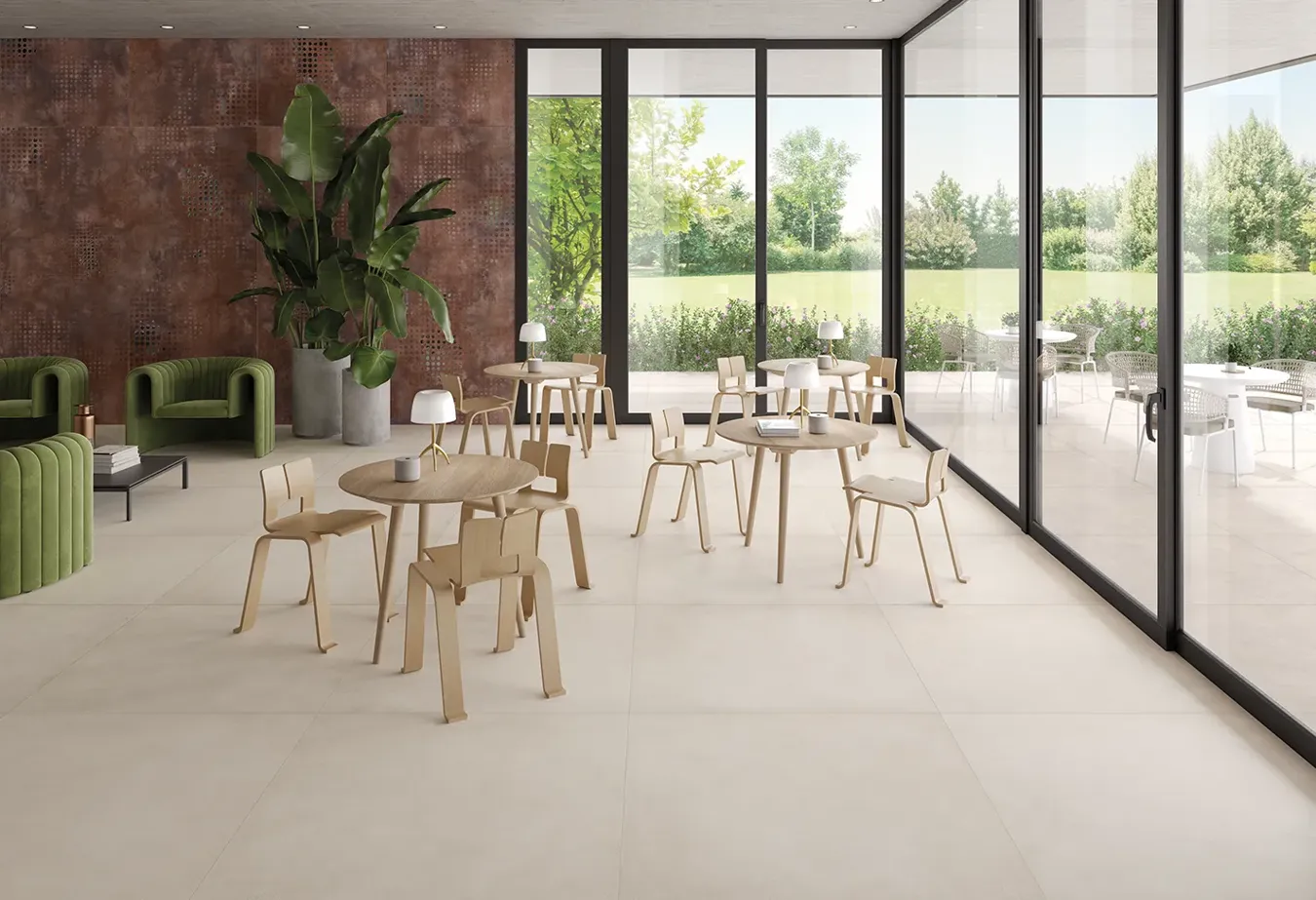 Contemporary communal area with beige tiled flooring, furnished with light wood tables and chairs, overlooking an outdoor garden through expansive glass windows.