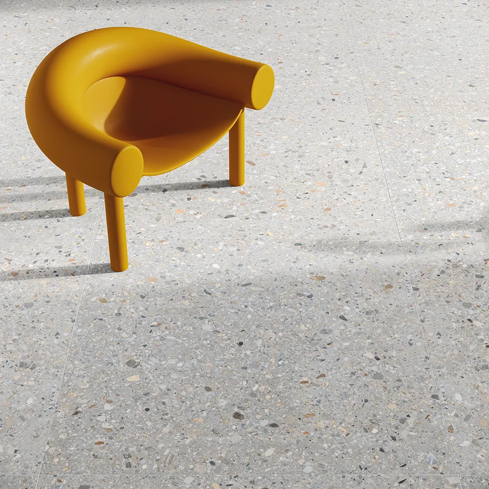 Pavimento effetto pietra con piastrelle grandi 120x120 cm, valorizzato da una sedia design gialla.