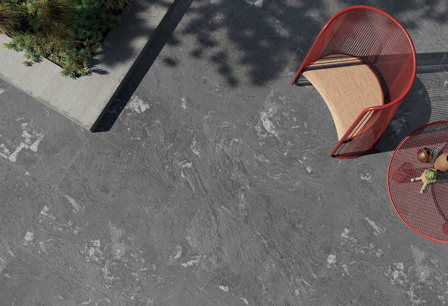 Dettaglio di pavimento esterno in gres porcellanato effetto pietra, con poltrona design rosso e tavolino da caffè.