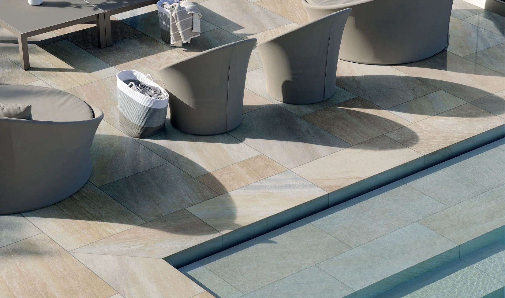 Terrazza moderna con pavimento in gres porcellanato quarzite beige della collezione Midlake colore Quartz, completa di divani e tavolo da esterno.