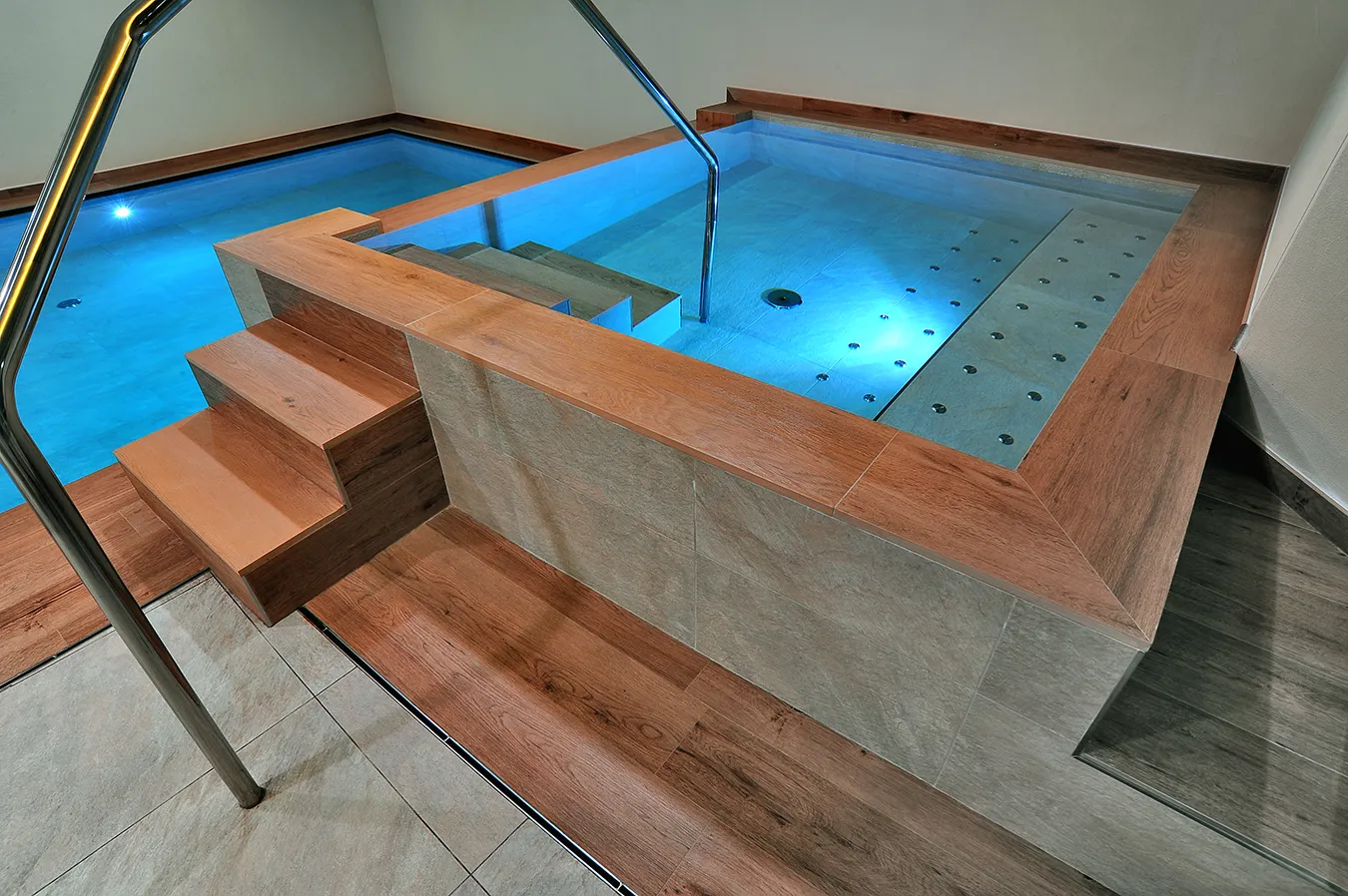 Sophisticated indoor hydrotherapy pool with wood-effect tiles from the Evoke collection, merging elegance with functionality in a wellness environment.