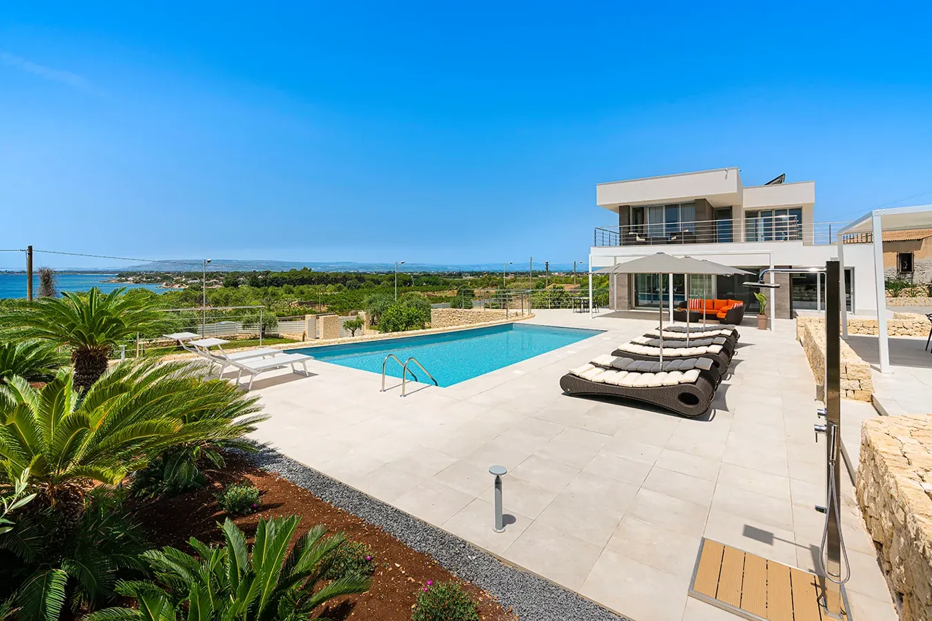 Outdoor pool with anti-slip porcelain stoneware flooring from the Noord collection in White, furnished terrace, and panoramic view.